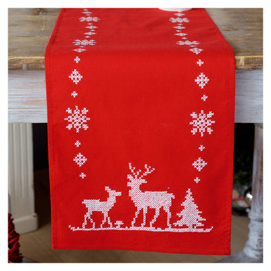 Red table runner with white reindeer and snowflake pattern on a wooden surface.