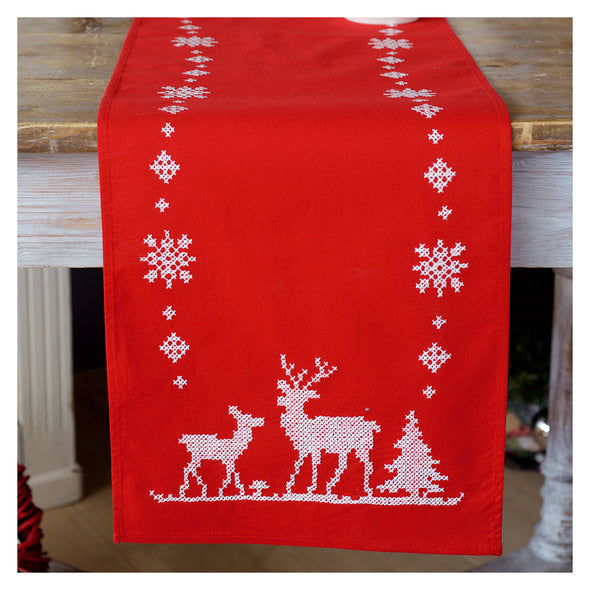 Red table runner with white reindeer and snowflake pattern on a wooden surface.