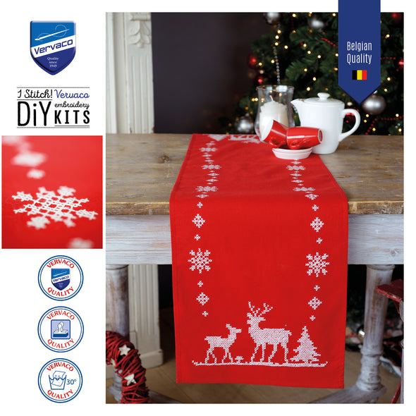 Red table runner with white reindeer and tree design on a wooden table, surrounded by Vervaco branding.