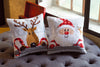 Two cross-stitched pillows featuring a reindeer and Santa Claus on a gray cushion.