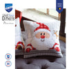 Cross-stitched Santa Claus pillow on a couch with Vervaco branding.
