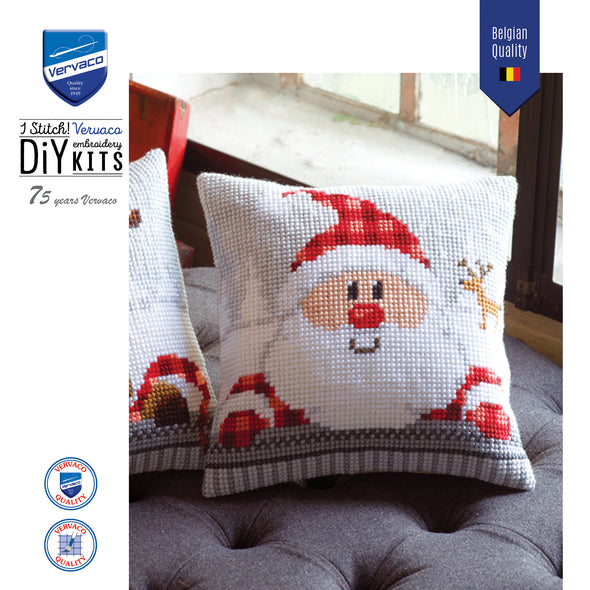 Cross-stitched Santa Claus pillow on a couch with Vervaco branding.