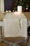 Beige embroidered table runner on a wooden table with candles and Christmas decorations in the background.