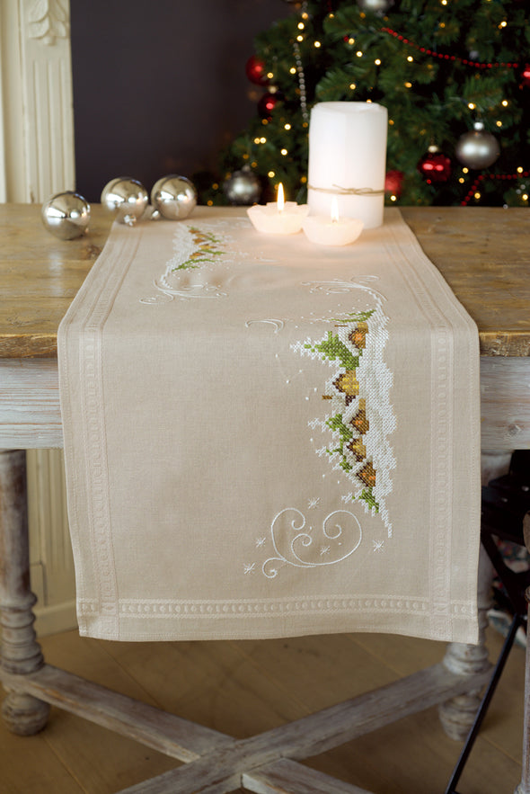 Beige embroidered table runner on a wooden table with candles and Christmas decorations in the background.